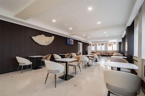 Un espace de restauration moderne avec des tables et des chaises, un élément décoratif mural et un coin salon à l’arrière-plan.