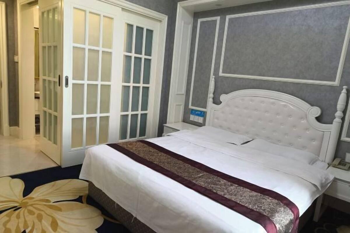 A bedroom with a white bed, a patterned throw, a white headboard, and a door with frosted glass panels.