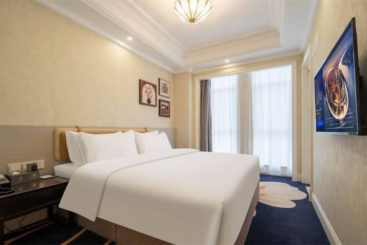 A hotel room with a large bed, a desk, a chair, a television, and a window with curtains.
