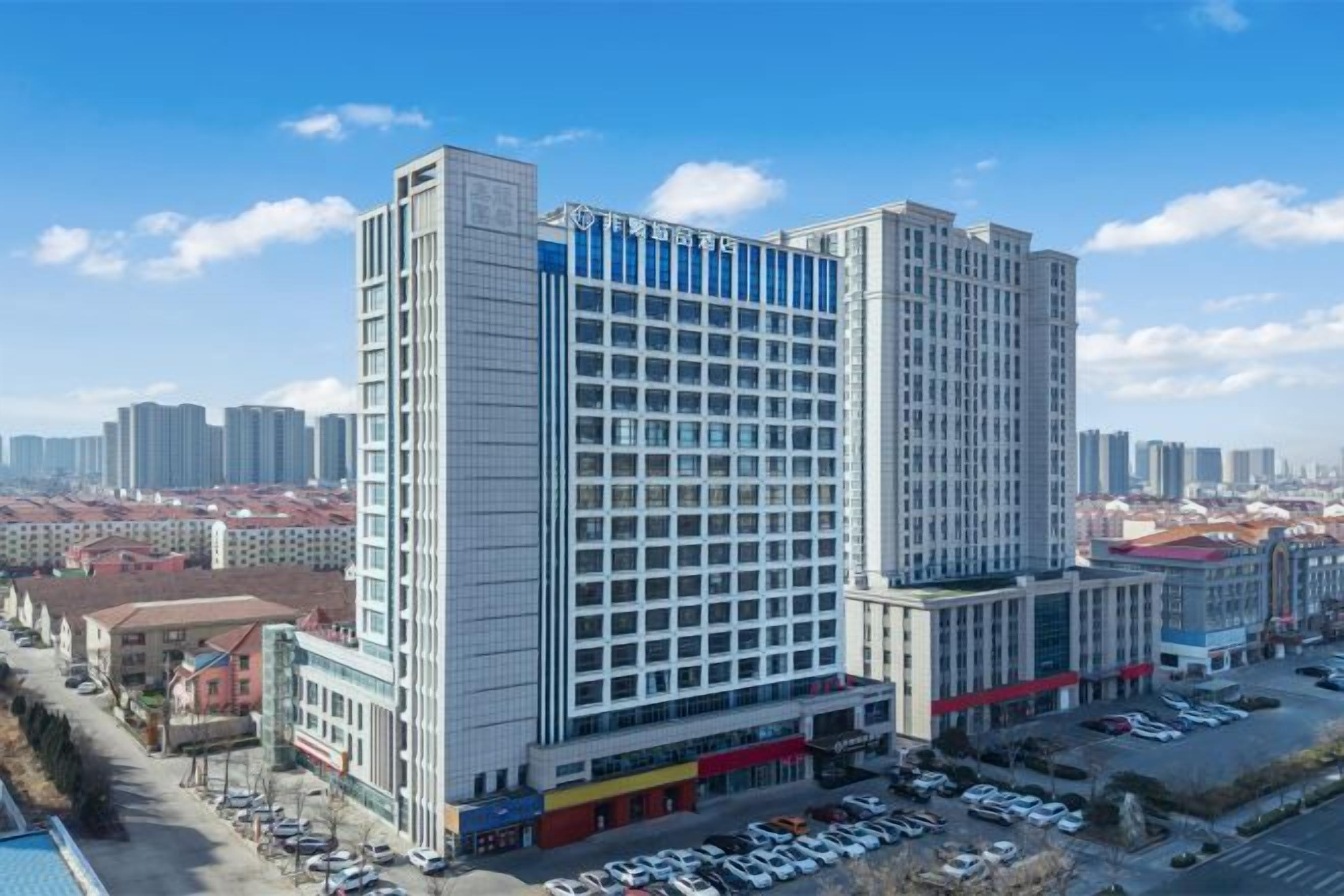 A high-rise hotel with multiple floors, a parking area in front, and a clear view of the surrounding cityscape.