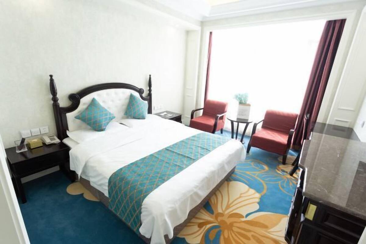 A hotel room with a bed, a red chair, a small table, and a view of the outdoors.