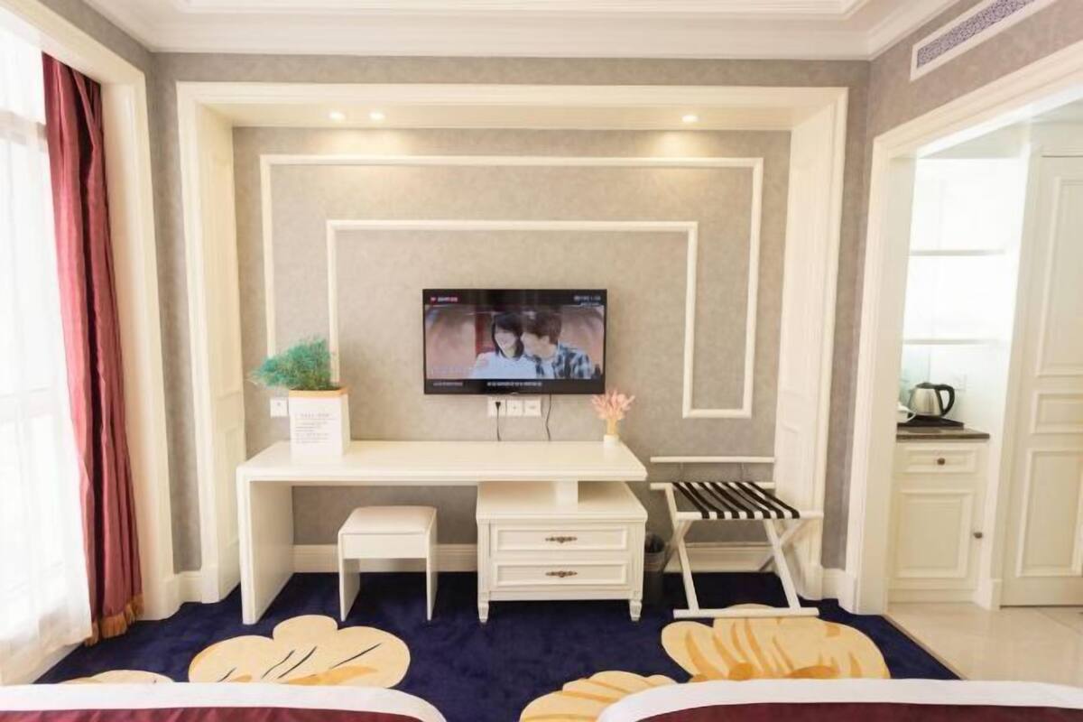 A bedroom with a bed, a desk, a chair, a TV, and a small plant.
