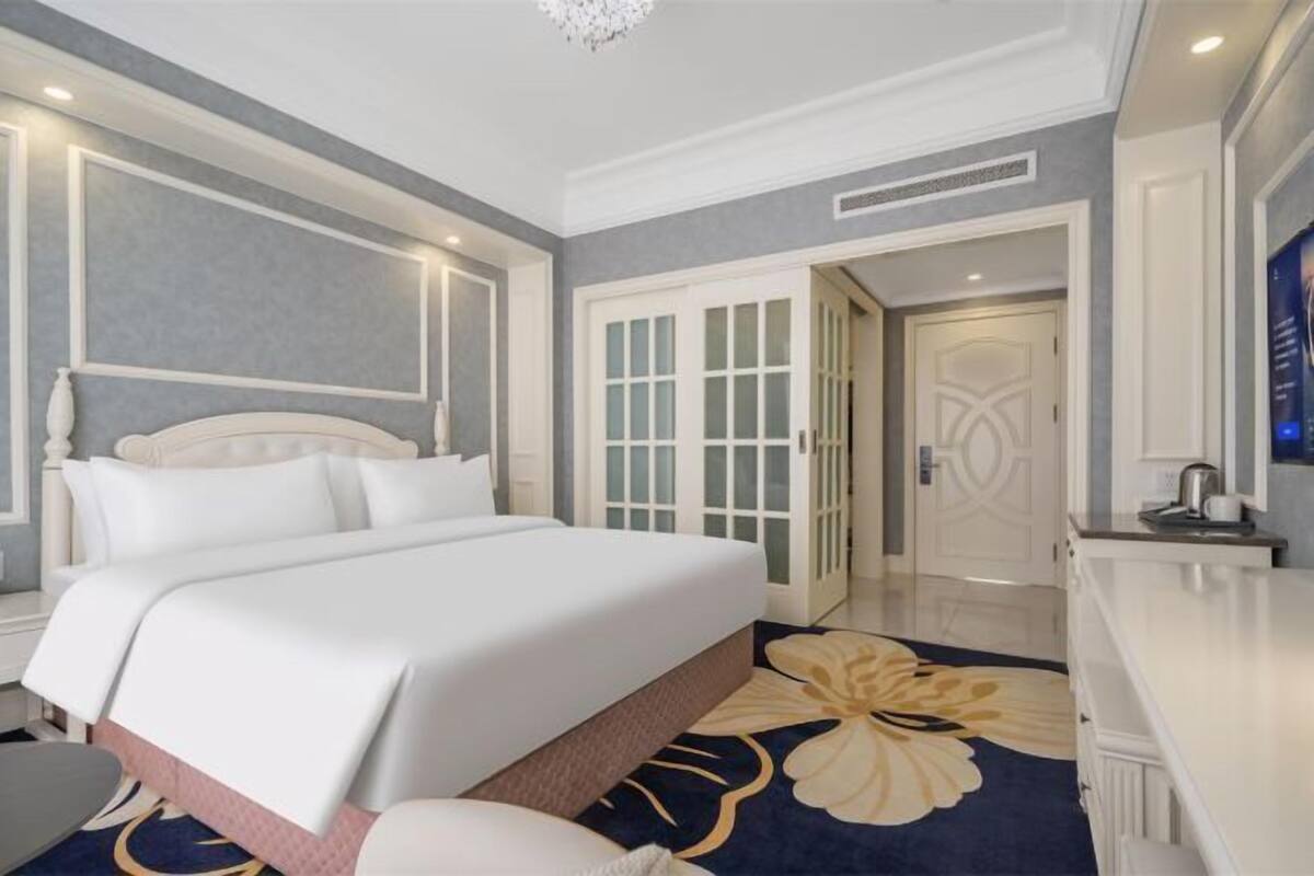A hotel room with a large bed, a desk, and a door leading to another room.