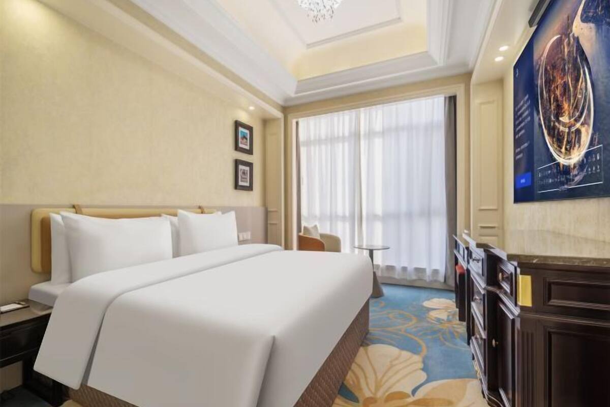 A hotel room with a large bed, a small table, a chair, and a painting on the wall.