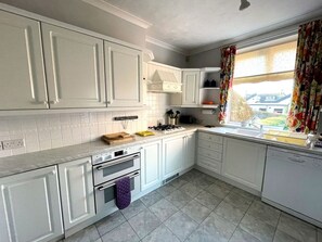 A modern kitchen with white cabinets, a gas stove, a built-in oven, and a window with floral curtains.