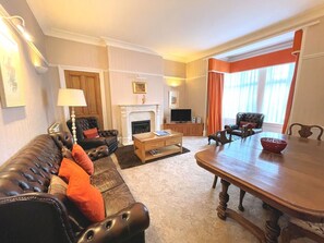 A living room with a fireplace, leather sofa, dining table, and a television. - Beautiful Period Property in Central Location - Pass the Keys (Dumfries)
