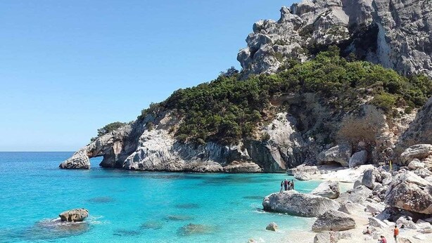 Eine felsige Küstenlinie mit klarem, türkisblauem Wasser und einer kleinen Strandbucht.