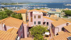 Eine Küstenstadt mit Häusern mit Terrakotta-Dächern, einer Marina mit Booten und weiter Sicht auf Meer und Berge im Hintergrund.