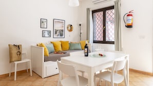 Ein modernes Wohnzimmer mit einem weißen Sofa, einem Esstisch und einem weißen Stuhl. Eine Feuerlöschvorrichtung ist an der Wand angebracht.