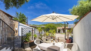 An outdoor patio with a table set for dining, surrounded by white chairs and a large umbrella. - Tradewinds Family House (Tortolì)