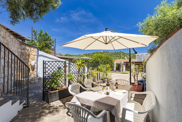 An outdoor patio with a table set for dining, surrounded by white chairs and a large umbrella.
