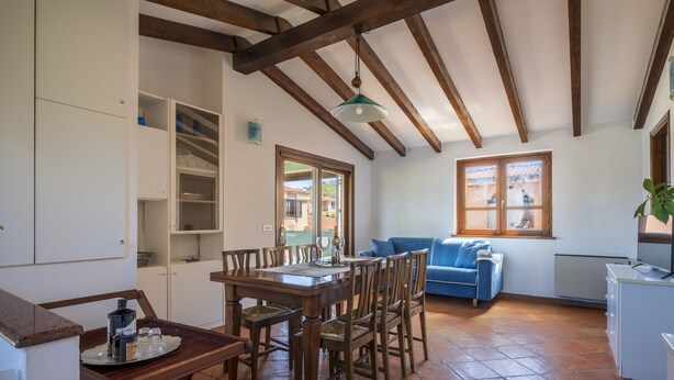 A spacious kitchen with a dining table and chairs, a blue sofa, and a view through the windows. - Il GECO Holiday Home (Tortoli')