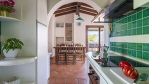 A kitchen with a dining area, featuring a tiled backsplash, wooden ceiling beams, and a central island with a red pepper. - Il GECO Holiday Home (Tortoli')