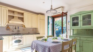 A kitchen with a dining table set for two, a stove, oven, and a window with a view of the outside. - Vacation House Summer By The Sea (Tortoli')