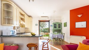 A kitchen with a microwave, stove, and a dining area with a table and chairs. - Vacation House Summer By The Sea (Tortoli')