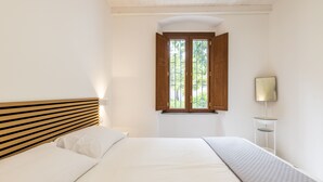 A bedroom with a wooden headboard, a bed with white bedding, a window with open shutters, and a bedside table with a lamp. - Casa Sulis Holiday Home (Tortoli')