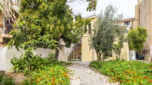 A pathway flanked by lush greenery and vibrant orange flowers, leading to a building with a staircase and a balcony. - Casa Sulis Holiday Home (Tortoli')