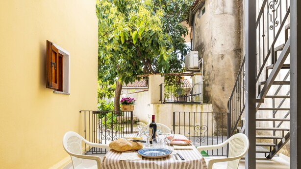 A table set for two with white chairs, a striped tablecloth, and a bottle of wine. - Casa Sulis Holiday Home (Tortoli')