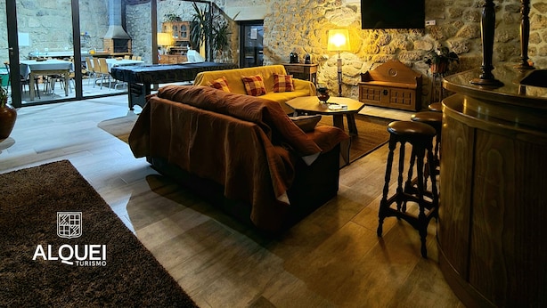 A cozy interior with a wooden ceiling, a sofa, a table, and a bar area. - Alqueiturismo - Garden House (Corujeira)