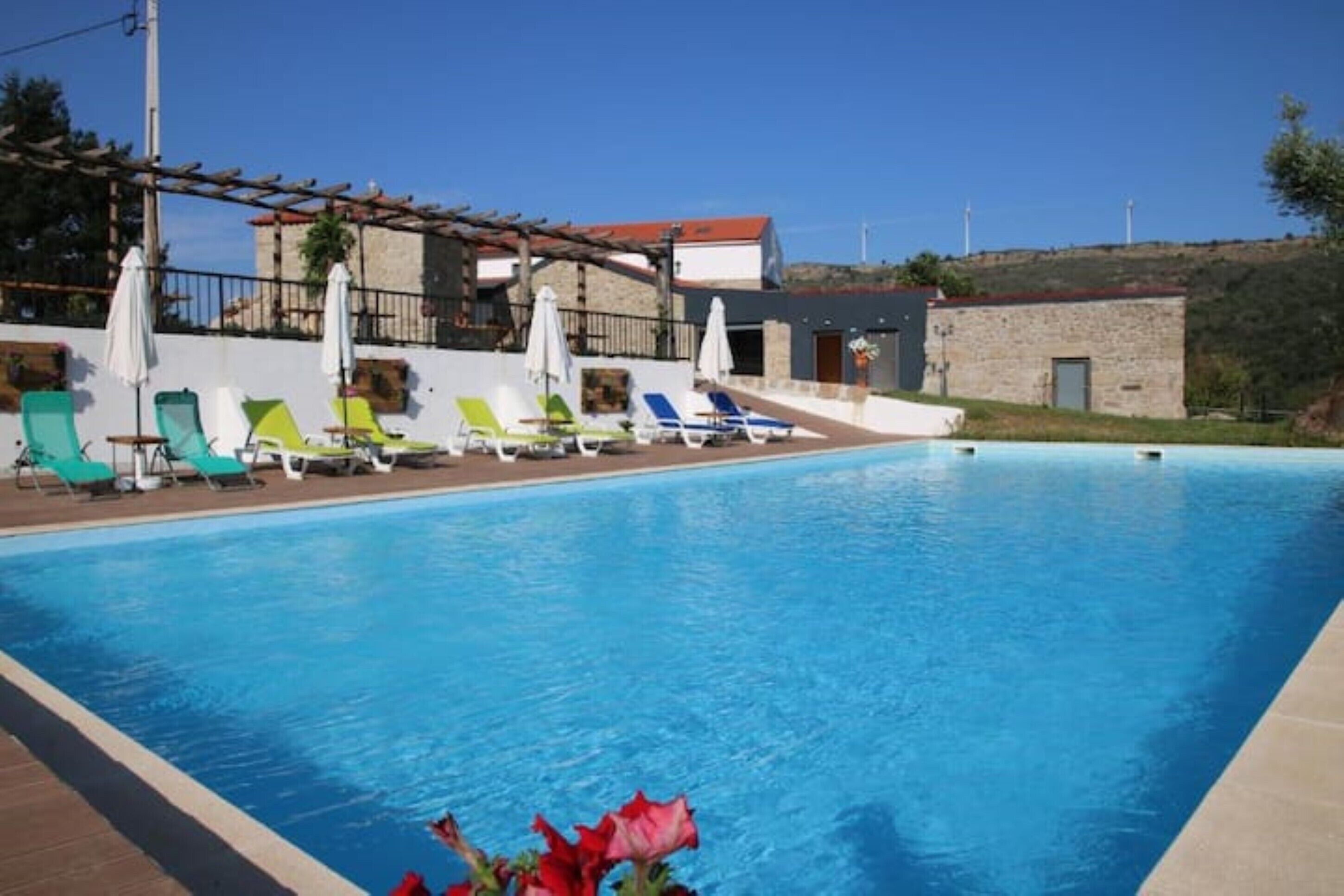 A swimming pool with lounge chairs and umbrellas, surrounded by stone buildings and a clear sky.