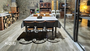 A rustic dining area with a stone wall, wooden ceiling, and a large table with chairs. - Alqueiturismo - Garden House (Corujeira)