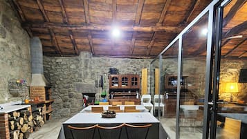 A rustic dining area with a stone wall, wooden ceiling, and a large table with chairs.