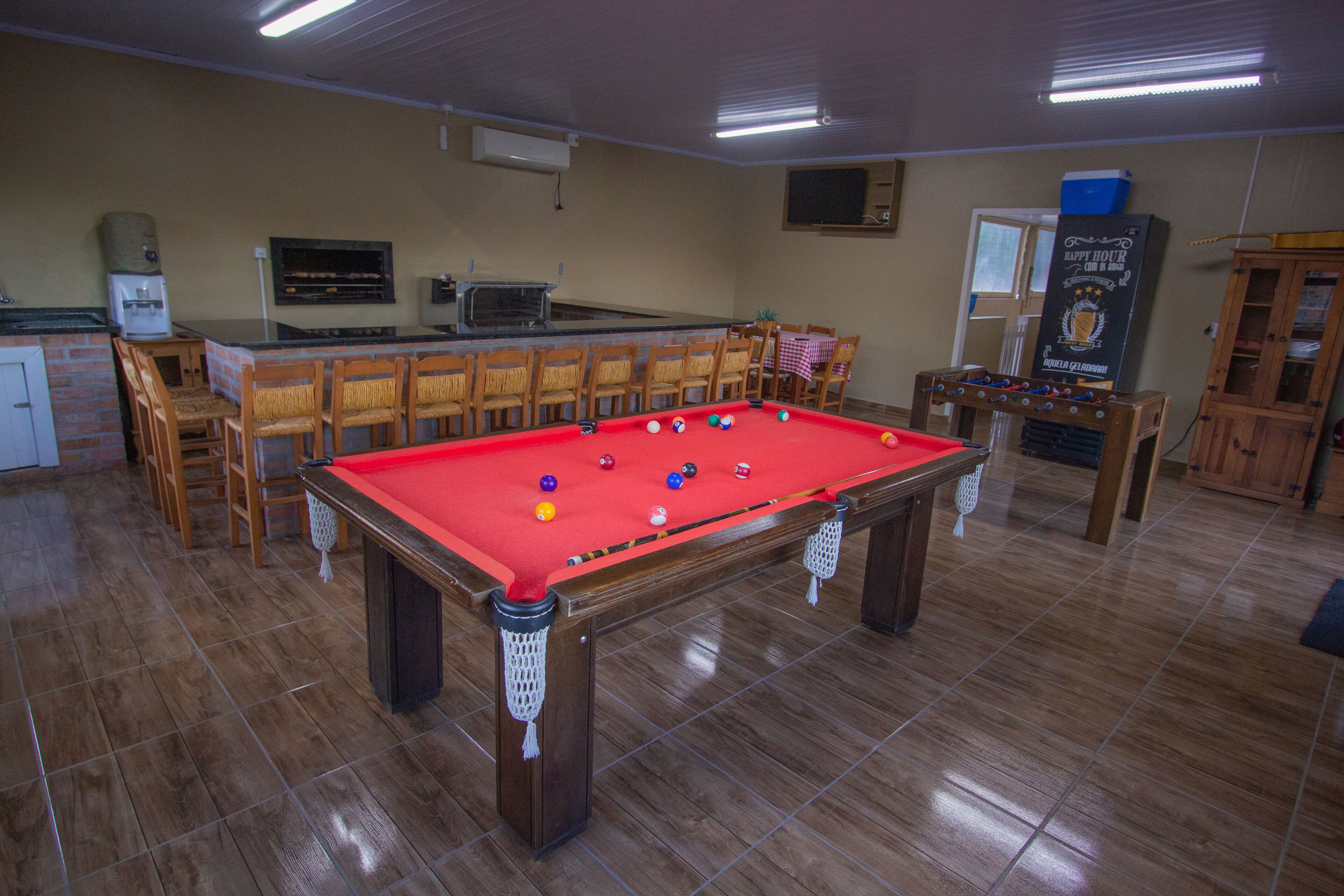 Uma mesa de bilhar em um espaço com bar, cadeiras e um armário.