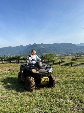 Une personne conduisant un véhicule tout-terrain dans un champ herbeux, avec des montagnes en arrière-plan.