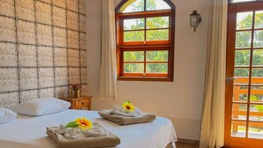 A hotel room with a large bed, a window with a view of greenery, and a wooden floor.