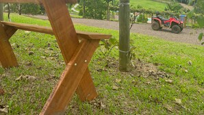 A wooden bench under a tree, a red ATV, and a grassy area with a building in the background.