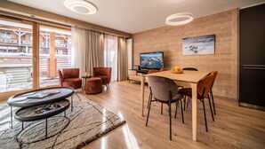 Un salon moderne avec un plancher en bois, une table à manger avec des chaises, un téléviseur et une grande fenêtre avec des rideaux.