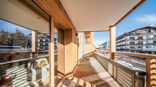 Un balcon en bois offrant une vue sur une montagne enneigée et sur un hôtel appelé « Le Galaxy ».