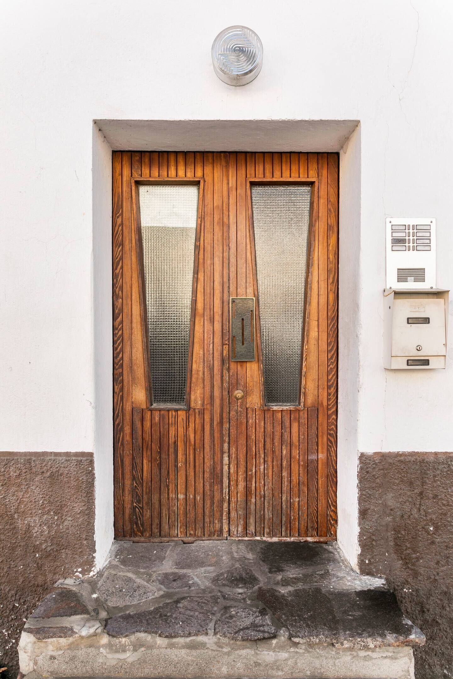 Une porte en bois avec une poignée en métal et deux panneaux de verre verticaux.