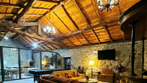 A cozy interior with a wooden ceiling, a sofa, a table, and a stone wall. - Alqueiturismo - House of the Coat of Arms (Corujeira)