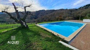 A swimming pool with a clear view of the surrounding landscape, including a tree and distant hills. - Alqueiturismo - House of the Coat of Arms (Corujeira)