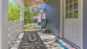 A covered porch with a wooden ceiling, a blue chair, and a patterned rug. - Luxury 1930s Reno'd Cape Cod, ❤️ of Midtown, 🐾, EV 🔌 (Memphis)