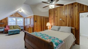 A bedroom with a wooden paneled wall, a bed with a quilt, a ceiling fan, and a window with a view. - Luxury 1930s Reno'd Cape Cod, ❤️ of Midtown, 🐾, EV 🔌 (Memphis)