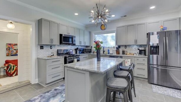 A modern kitchen with grey cabinetry, stainless steel appliances, and a central island with bar stools. - Luxury 1930s Reno'd Cape Cod, ❤️ of Midtown, 🐾, EV 🔌 (Memphis)