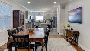 A spacious dining area with a wooden table and chairs, a kitchen in the background, and a large painting on the wall. - Luxury 1930s Reno'd Cape Cod, ❤️ of Midtown, 🐾, EV 🔌 (Memphis)