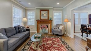 A living room with a fireplace, a sofa, a coffee table, and a dining area. - Luxury 1930s Reno'd Cape Cod, ❤️ of Midtown, 🐾, EV 🔌 (Memphis)