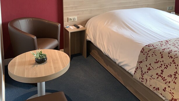 Habitación de hotel con cama, una silla, una mesita con una planta y dos luces en la pared.