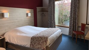 Una habitación de hotel con cama, armario, silla y ventana con cortinas.