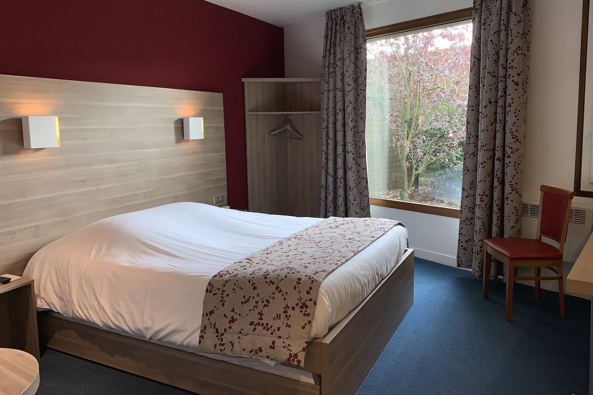 A hotel room with a bed, a wardrobe, a chair, and a window with curtains.