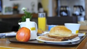 Bandeja de desayuno con tostadas, una taza de café, una botella de jugo y una manzana.