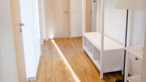 A hallway with wooden flooring, a white wardrobe with a mirror, and a floor lamp. - Modern and bright vacation apartment with Hutewald view (Vöhl)