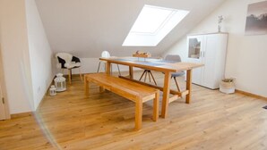A room with a wooden floor, a wooden table with a bench, a white cabinet, and a skylight. - Modern and bright vacation apartment with Hutewald view (Vöhl)