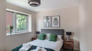 Quarto moderno com uma cama grande, almofadas verdes, duas mesas de cabeceira com luminárias e uma obra de arte na parede.