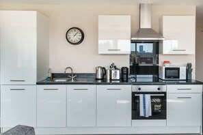 A modern kitchen with white cabinets, a stainless steel range hood, a microwave, and a kettle.