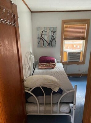 A small bedroom with a single bed, a wall-mounted bicycle art piece, and a window with blinds.