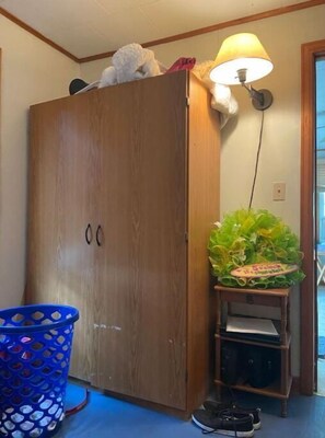 Une armoire en bois surmontée d’une lampe, un panier bleu et une petite étagère avec une plante.